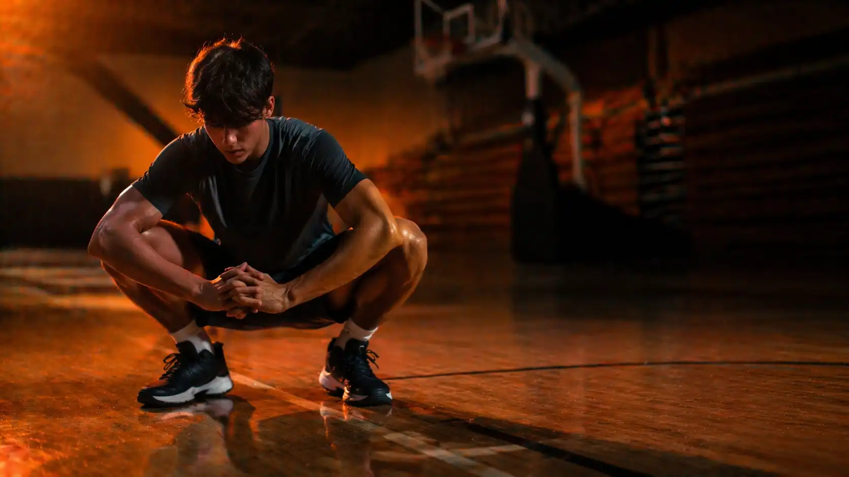 High school basketball player performing a deep squat mobility exercise on an indoor basketball court